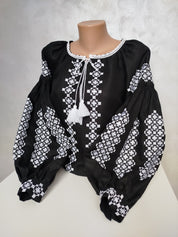 Women's Ukrainian Vyshyvanka, black homespun fabric blouse with intricate white embroidery and tassels, reflecting folk tradition.