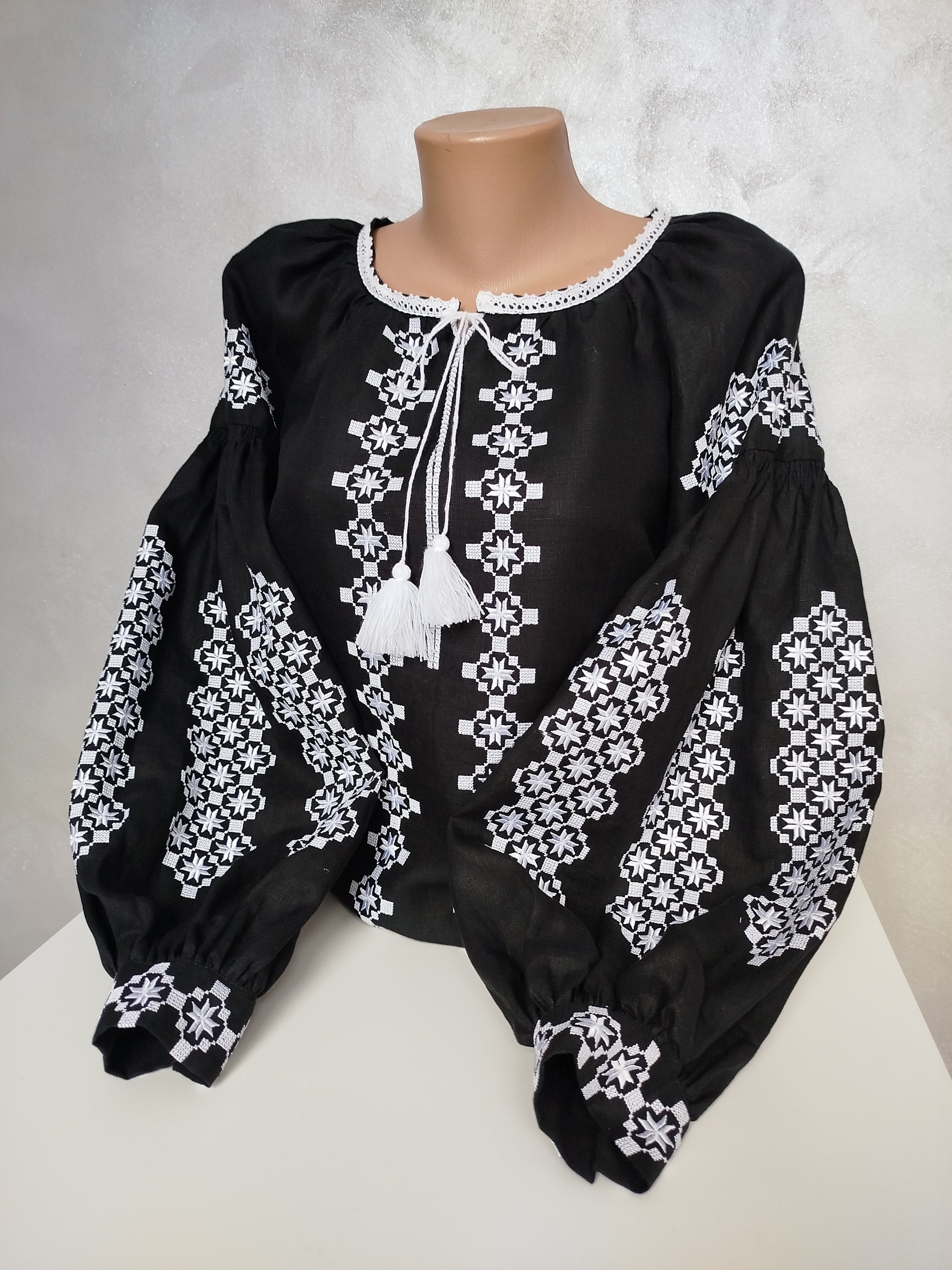 Women's Ukrainian Vyshyvanka, black homespun fabric blouse with intricate white embroidery and tassels, reflecting folk tradition.