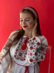 Woman wearing a traditional Ukrainian Vyshyvanka blouse with red and black embroidery on white fabric, against a red background.