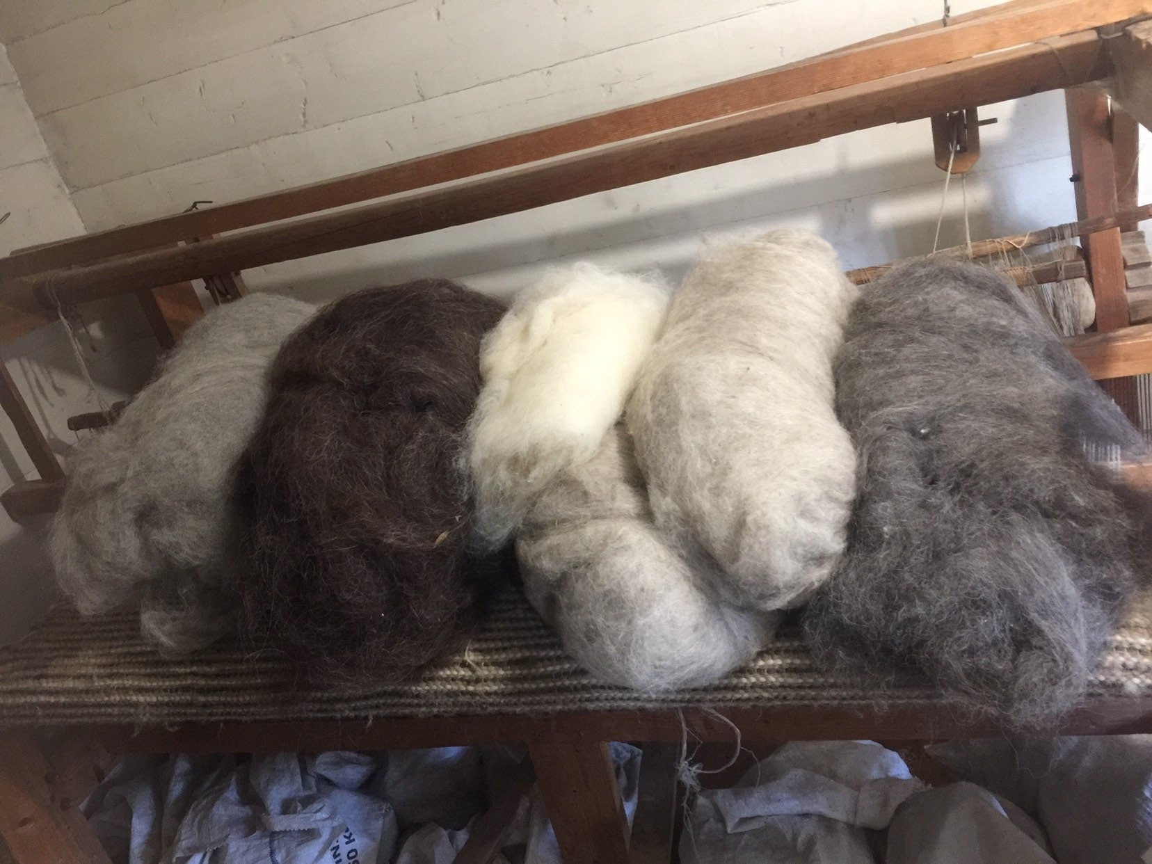 Piles of natural sheep wool in various colors ready for hand knitting on a wooden bench.