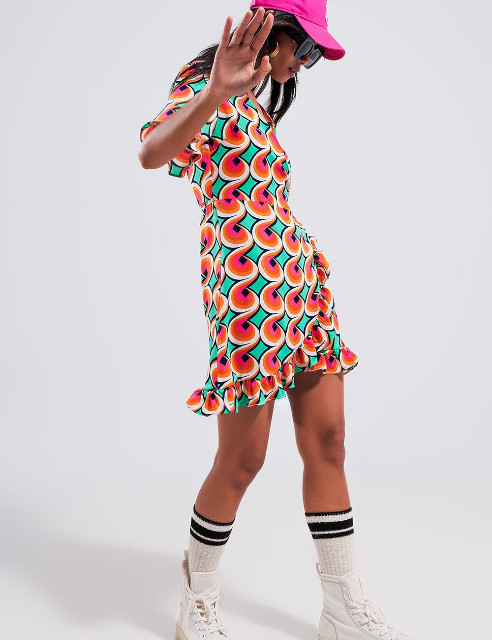 Model wearing Marisol 70s Wrap Ruffle Hem Mini Dress with bold orange geometric print, showcasing V-neckline and frill trim.