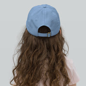 Child wearing blue youth baseball cap with adjustable strap, seen from the back, highlighting breathable design and long curly hair.