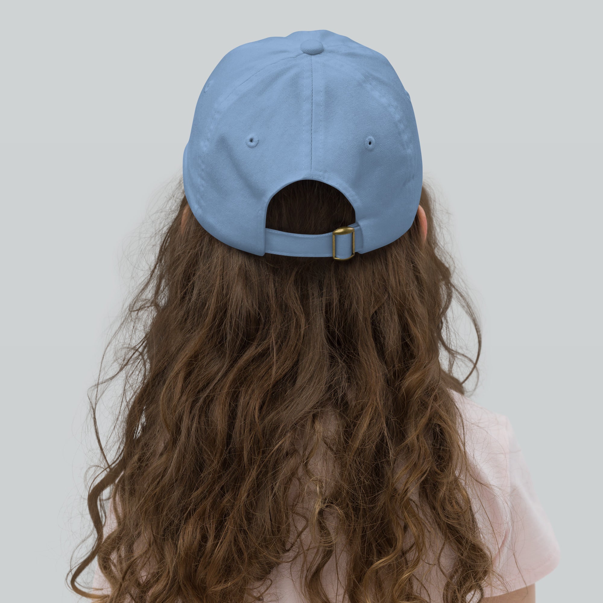 Child wearing blue youth baseball cap with adjustable strap, seen from the back, highlighting breathable design and long curly hair.