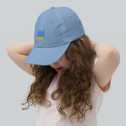 Girl wearing blue youth baseball cap with Ukrainian Tryzub emblem, featuring adjustable strap and breathable design for active kids.