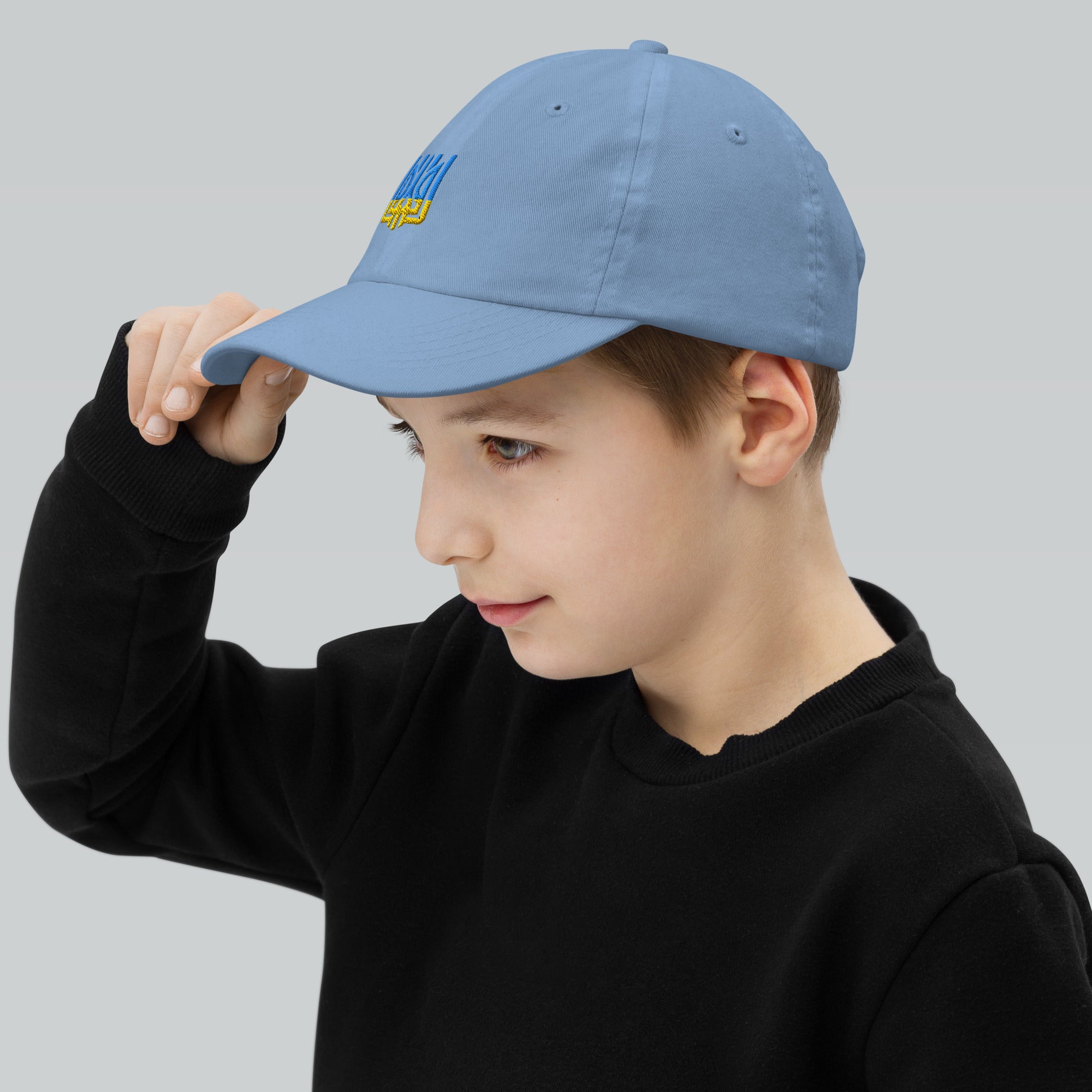 Youth wearing a blue baseball cap with Ukrainian Tryzub emblem, showcasing breathable, adjustable design for active kids.
