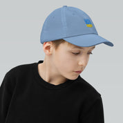 Youth baseball cap with Ukrainian Tryzub, adjustable and breathable, worn by a young boy, ideal for active kids, 100% cotton twill.
