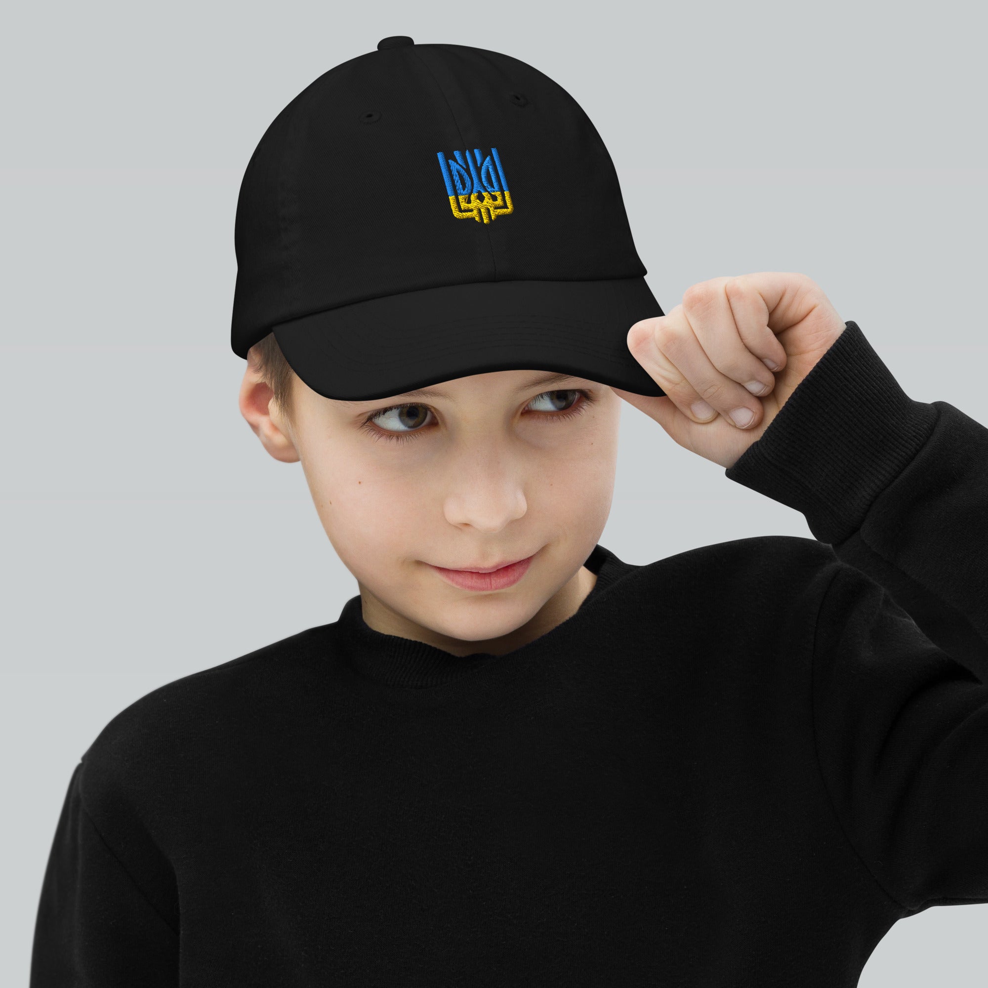 Boy wearing a youth baseball cap with Ukrainian Tryzub emblem, breathable and adjustable, perfect for active kids.