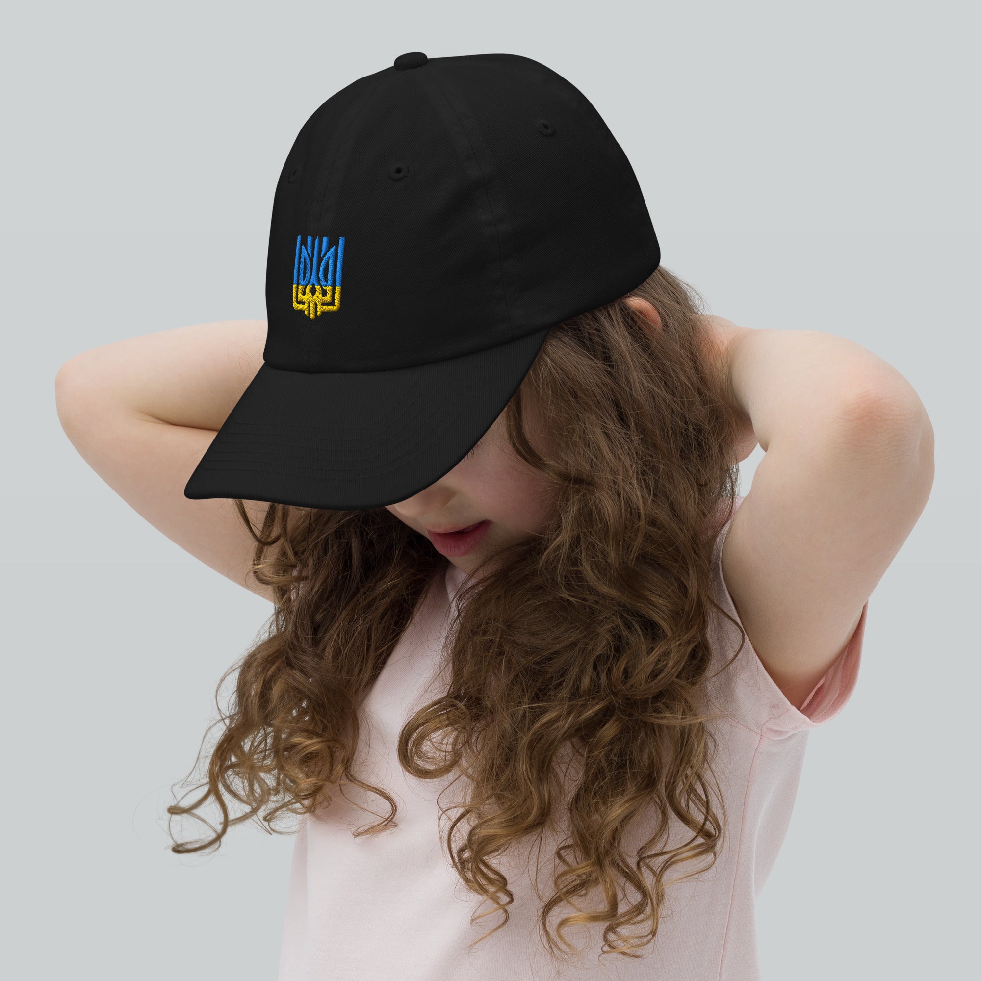 Girl wearing a youth baseball cap with Ukrainian Tryzub emblem, showing its breathable design and adjustable strap for active kids.