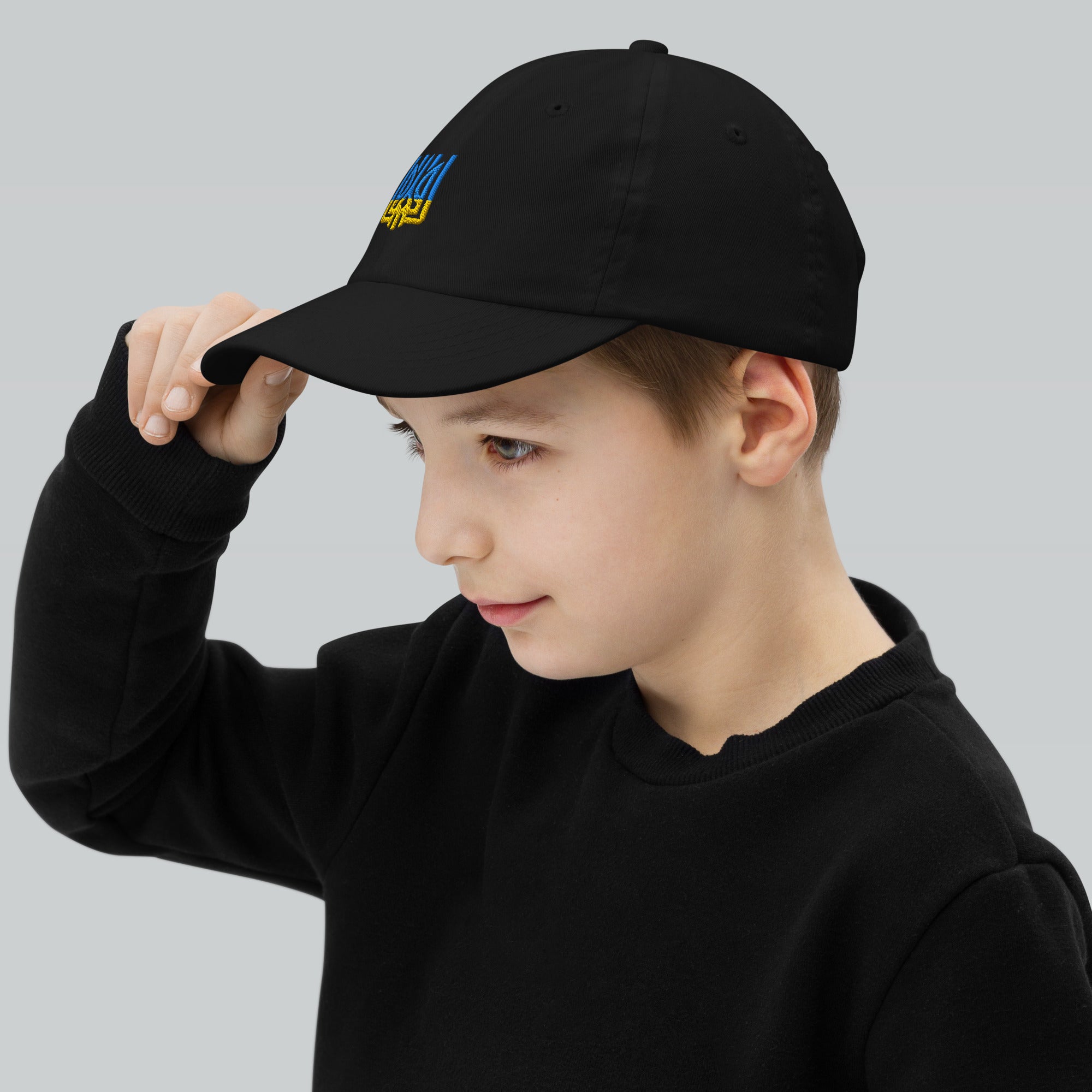 Child wearing a black youth baseball cap with Ukrainian Tryzub emblem, showcasing its adjustable fit and breathable design for active wear.
