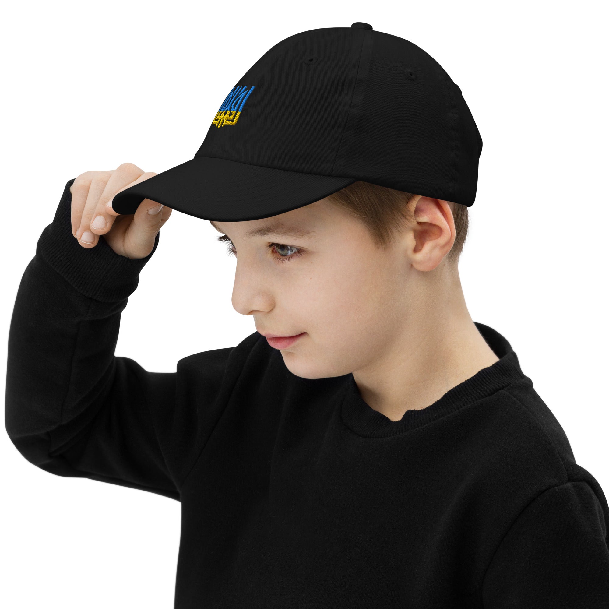 Young boy wearing a black youth baseball cap with Ukrainian Tryzub emblem, showing adjustable fit and breathable design, in a casual outfit.
