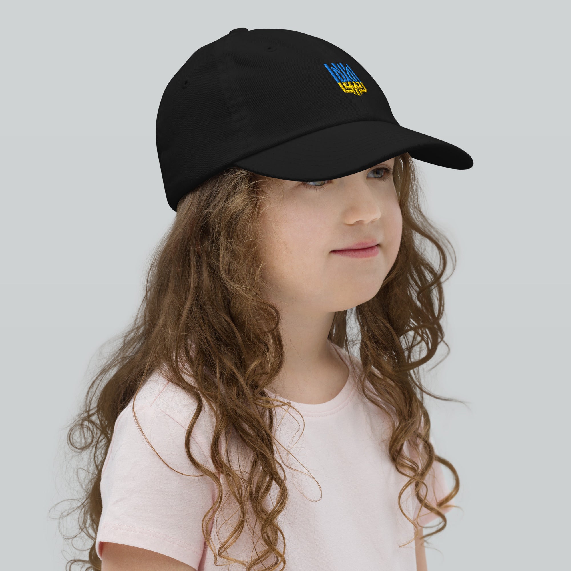 Girl wearing a youth baseball cap with Ukrainian Tryzub emblem, perfect for sports and outdoor activities. Breathable and adjustable for active kids.