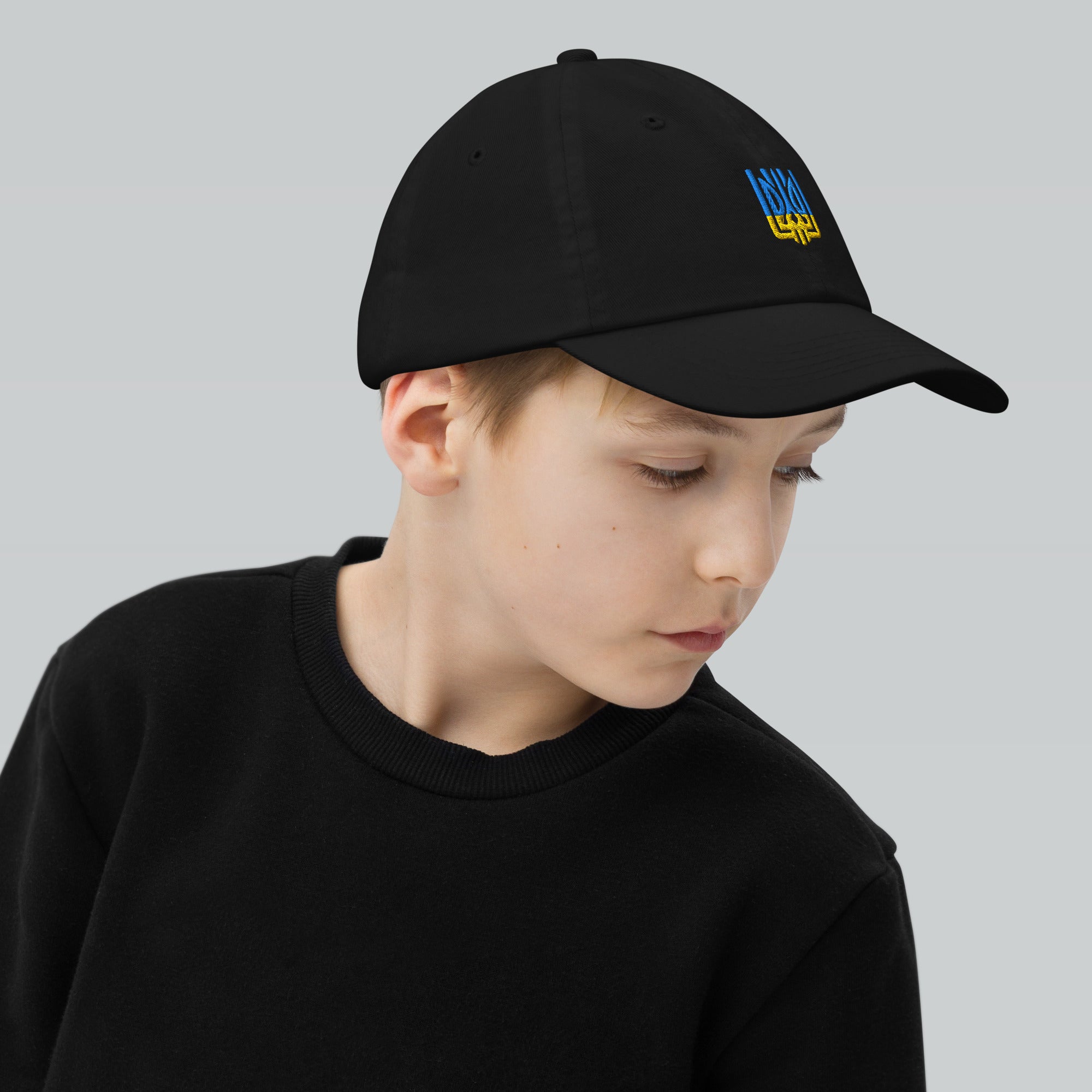 Youth wearing black baseball cap with Ukrainian Tryzub, breathable and adjustable, ideal for active kids outdoors and sports.