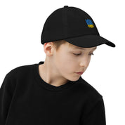 Youth wearing black baseball cap with Ukrainian Tryzub emblem, made from bio-washed cotton twill, features ventilation eyelets and adjustable strap.