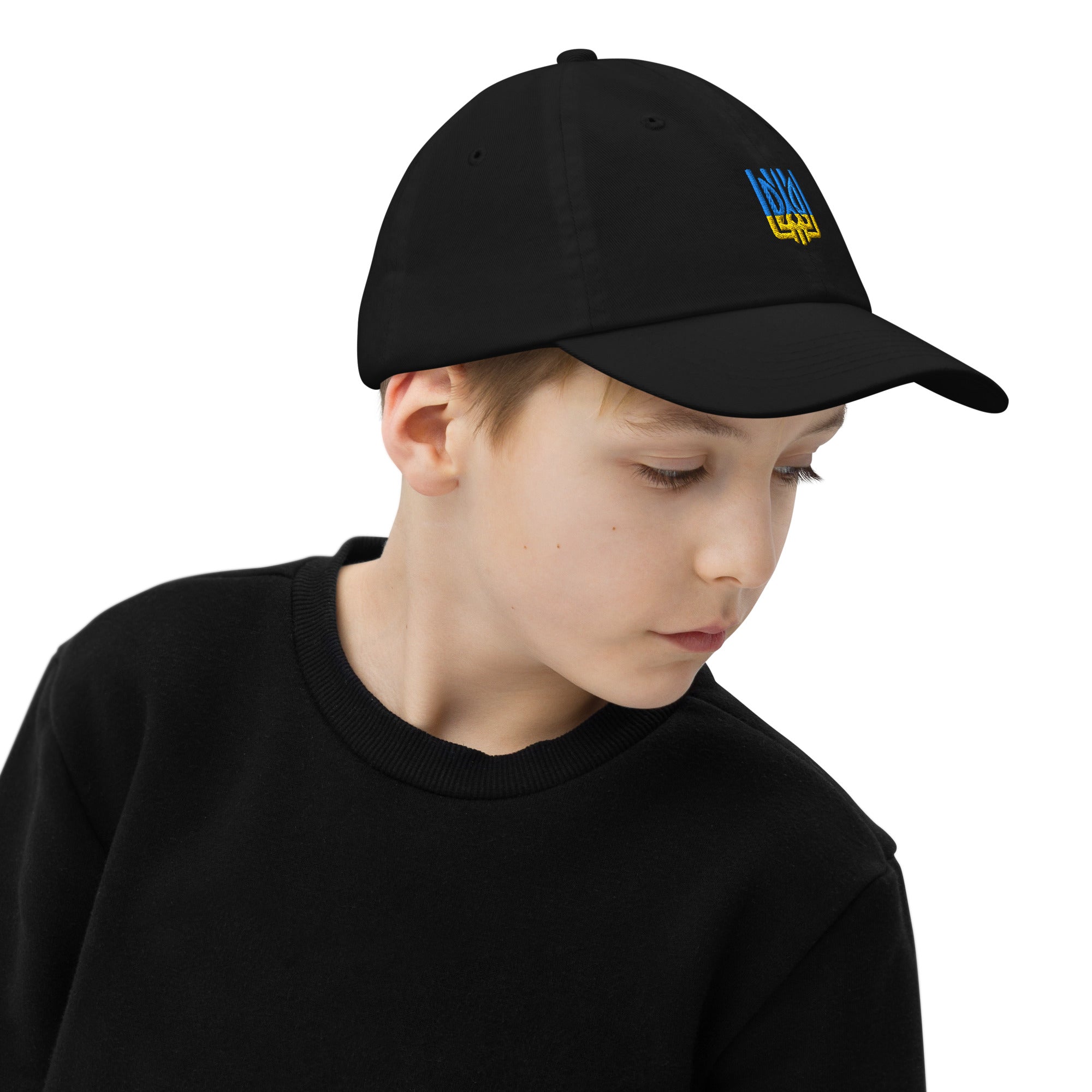 Youth wearing black baseball cap with Ukrainian Tryzub emblem, made from bio-washed cotton twill, features ventilation eyelets and adjustable strap.