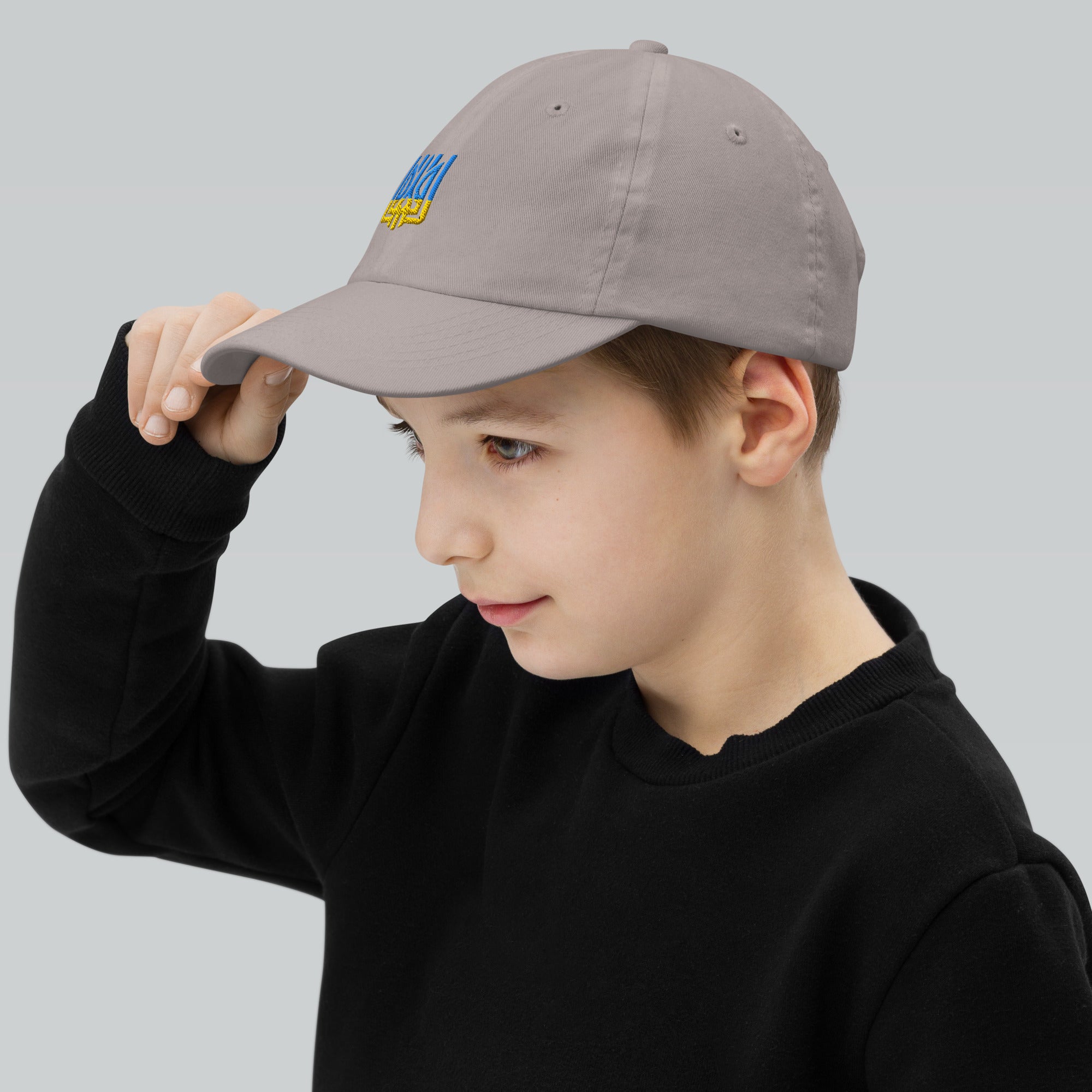 Youth wearing adjustable baseball cap featuring Ukrainian Tryzub, made of soft bio-washed cotton, ideal for active kids' outdoor adventures.