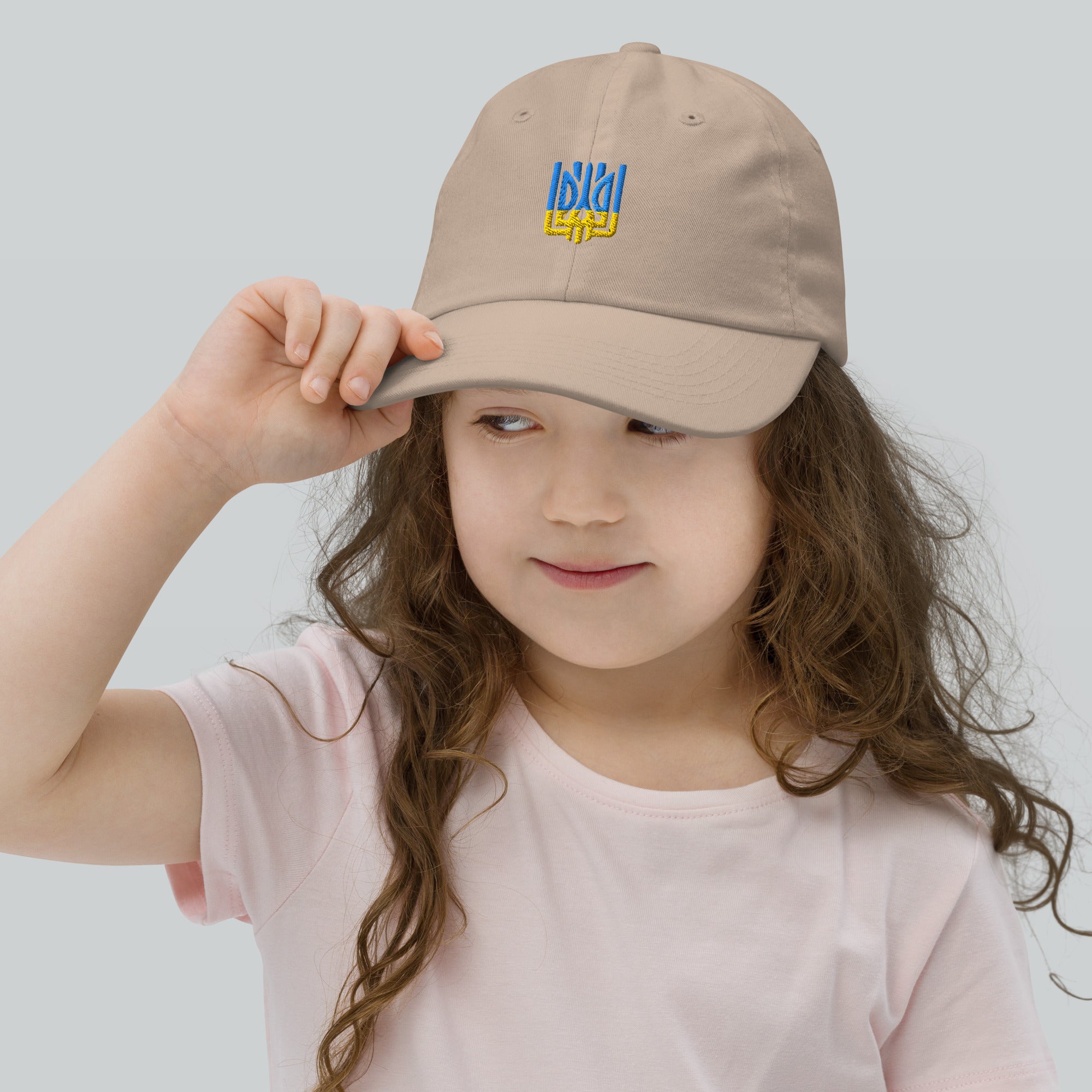 Youth wearing adjustable baseball cap with Ukrainian Tryzub emblem. Chino cotton twill for comfort. Perfect for active kids.