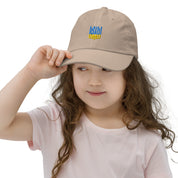 Young girl wearing a beige youth baseball cap with Ukrainian Tryzub emblem, showcasing breathable and adjustable design for active kids.