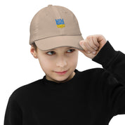 Young boy wearing a beige youth baseball cap with Ukrainian Tryzub emblem, showcasing adjustable fit and breathability.