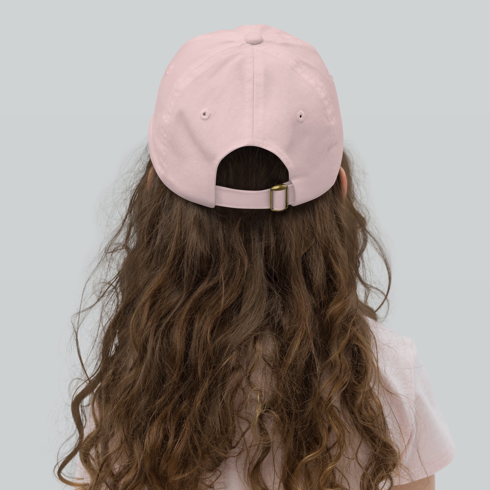 Back view of a child wearing a pink youth baseball cap, featuring an adjustable strap and ventilation eyelets, perfect for active outdoor play.