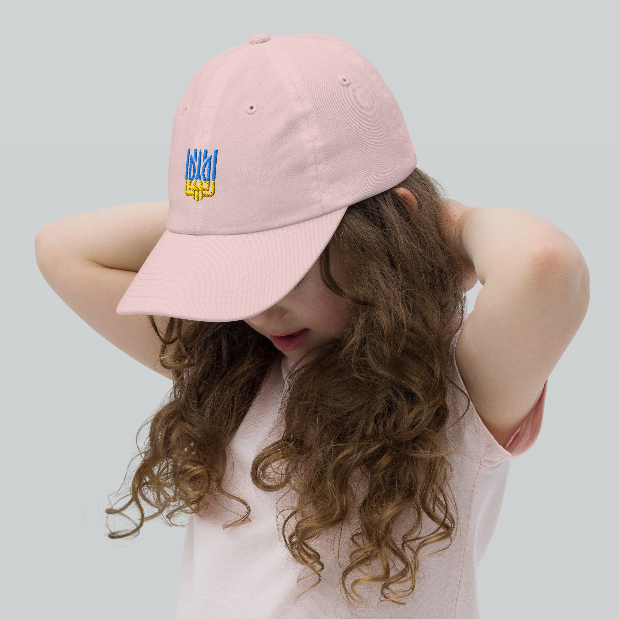 Girl wearing pink youth baseball cap with Ukrainian Tryzub emblem, ideal for active kids, adjustable and breathable design.