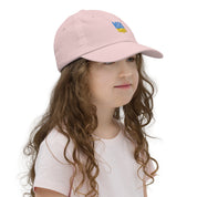 Young girl wearing a pink youth baseball cap with Ukrainian Tryzub emblem, made from bio-washed chino cotton, featuring an adjustable strap and ventilation.