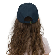 Back view of a child wearing a navy blue adjustable baseball cap with Ukrainian Tryzub, showcasing long hair and casual attire.