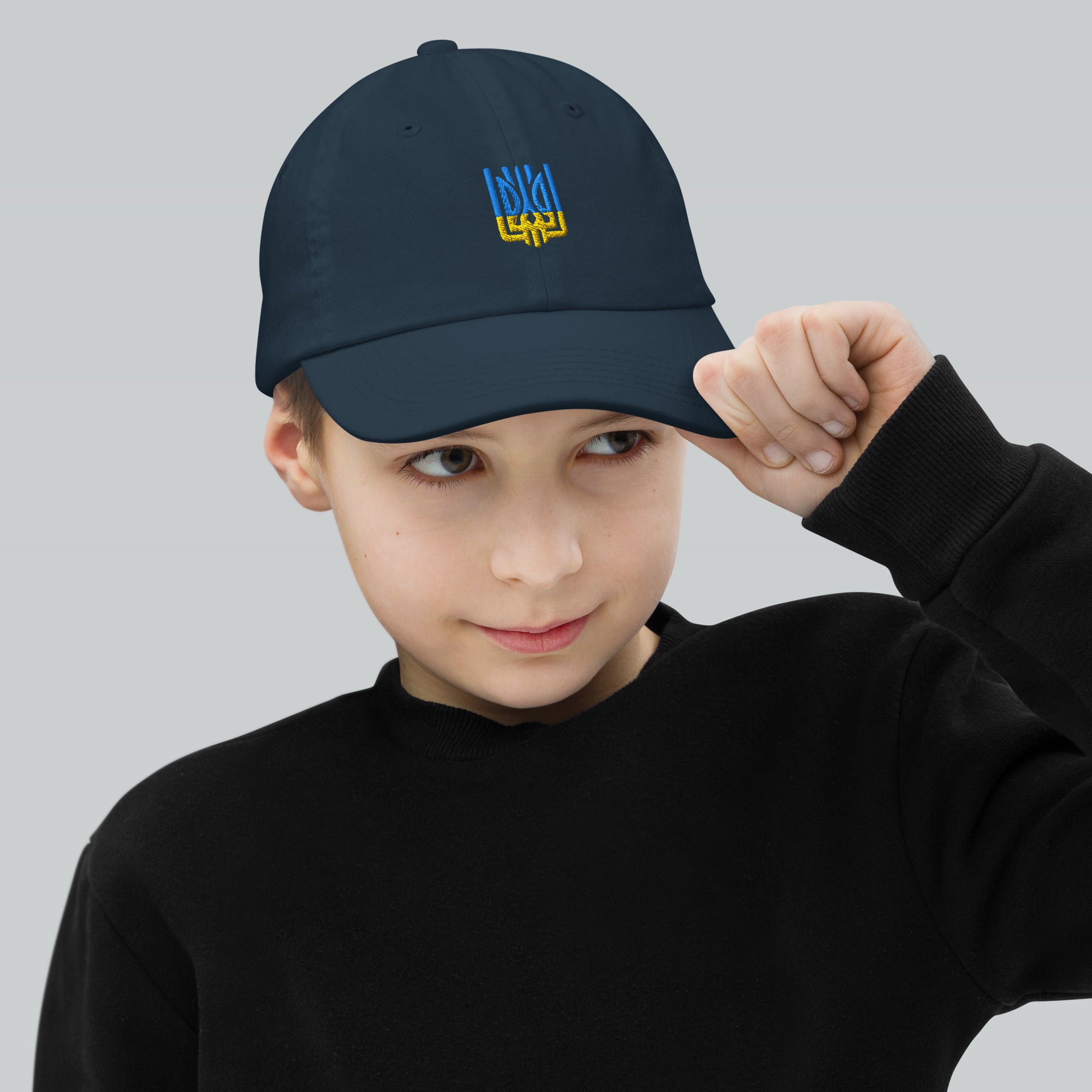 Youth wearing adjustable baseball cap with Ukrainian Tryzub emblem, ideal for active kids. Made of bio-washed chino cotton twill.