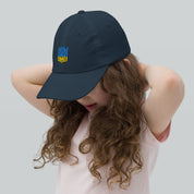 Girl wearing youth baseball cap with Ukrainian Tryzub emblem, breathable and adjustable for active kids, made from chino cotton twill.