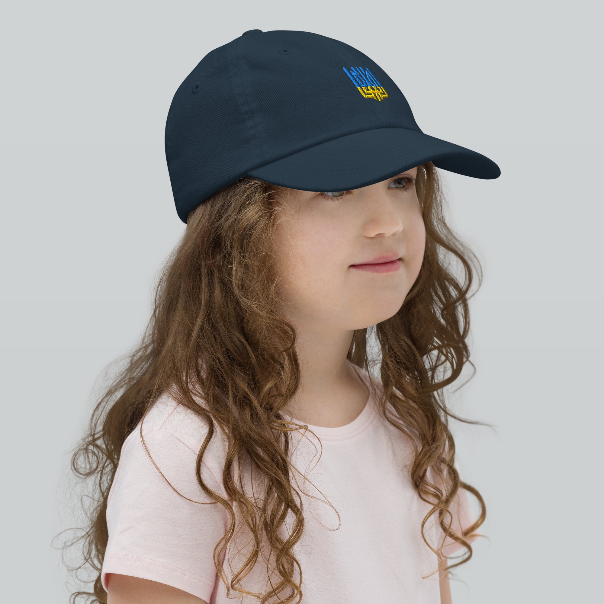 Youth baseball cap with Ukrainian Tryzub emblem on girl, breathable and adjustable for perfect fit and comfort.