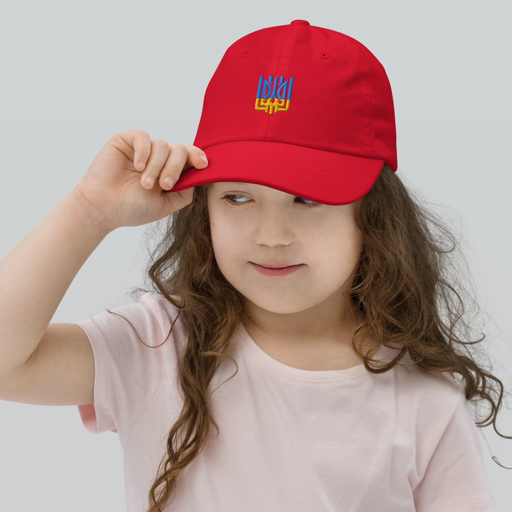 Child wearing red youth baseball cap with Ukrainian Tryzub emblem, perfect for active kids. Made of bio-washed chino cotton twill.