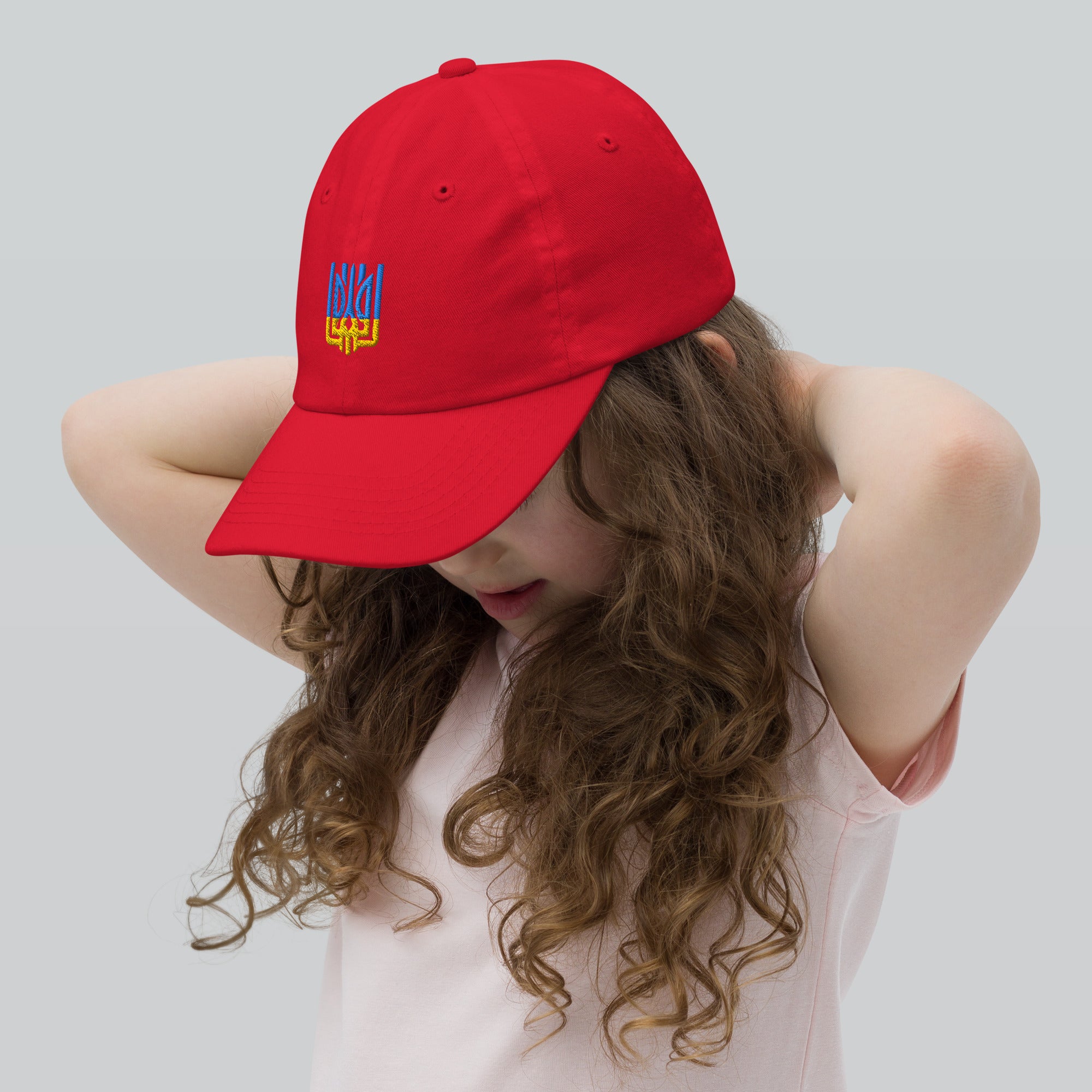 Child wearing a red youth baseball cap with Ukrainian Tryzub emblem, featuring breathable fabric and an adjustable strap for active kids.