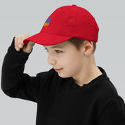 Youth wearing red baseball cap with Ukrainian Tryzub emblem, adjustable fit for active kids, made from bio-washed chino cotton twill.