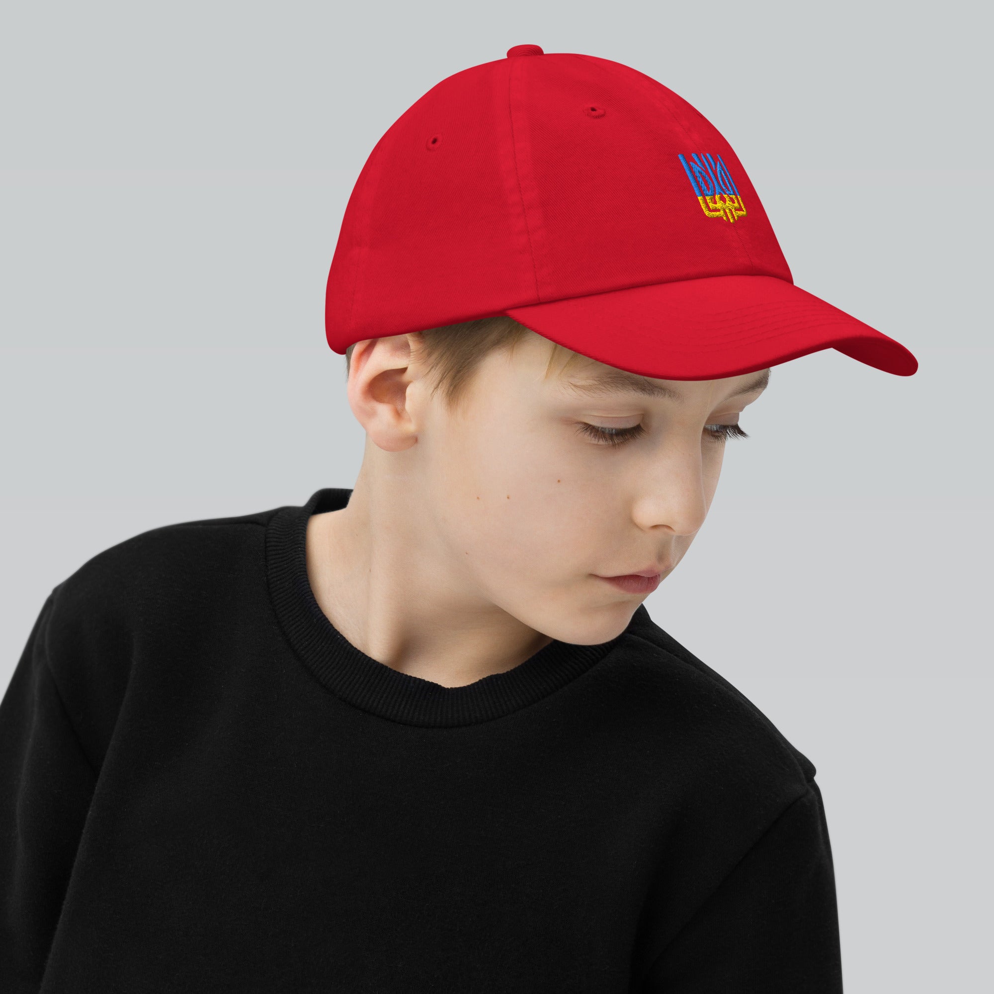 Youth wearing red baseball cap with Ukrainian Tryzub emblem, breathable and adjustable for active play