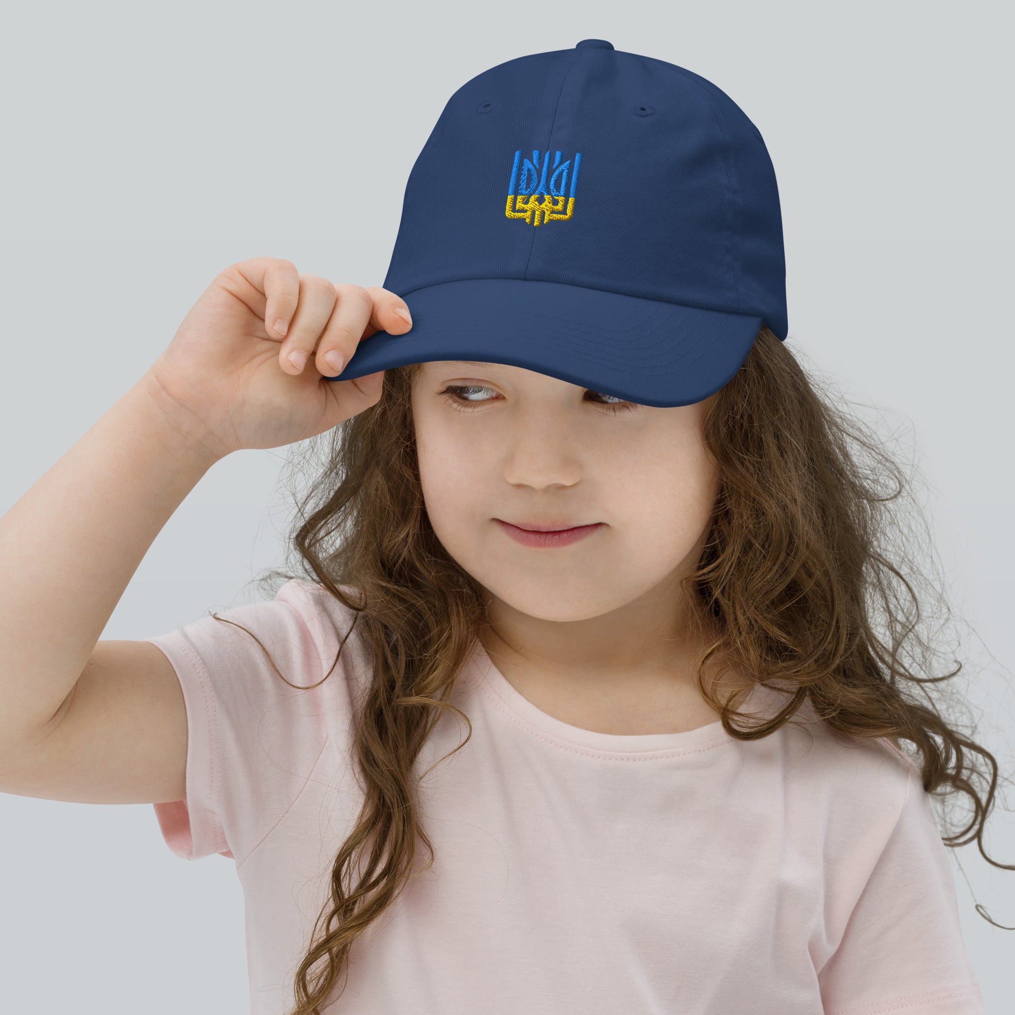 Child wearing blue baseball cap with Ukrainian Tryzub emblem; cap is breathable and adjustable, ideal for active kids and outdoor play.