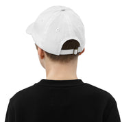 Back view of a youth wearing a white baseball cap with an adjustable strap and ventilation eyelets, shown on a child wearing a black shirt.