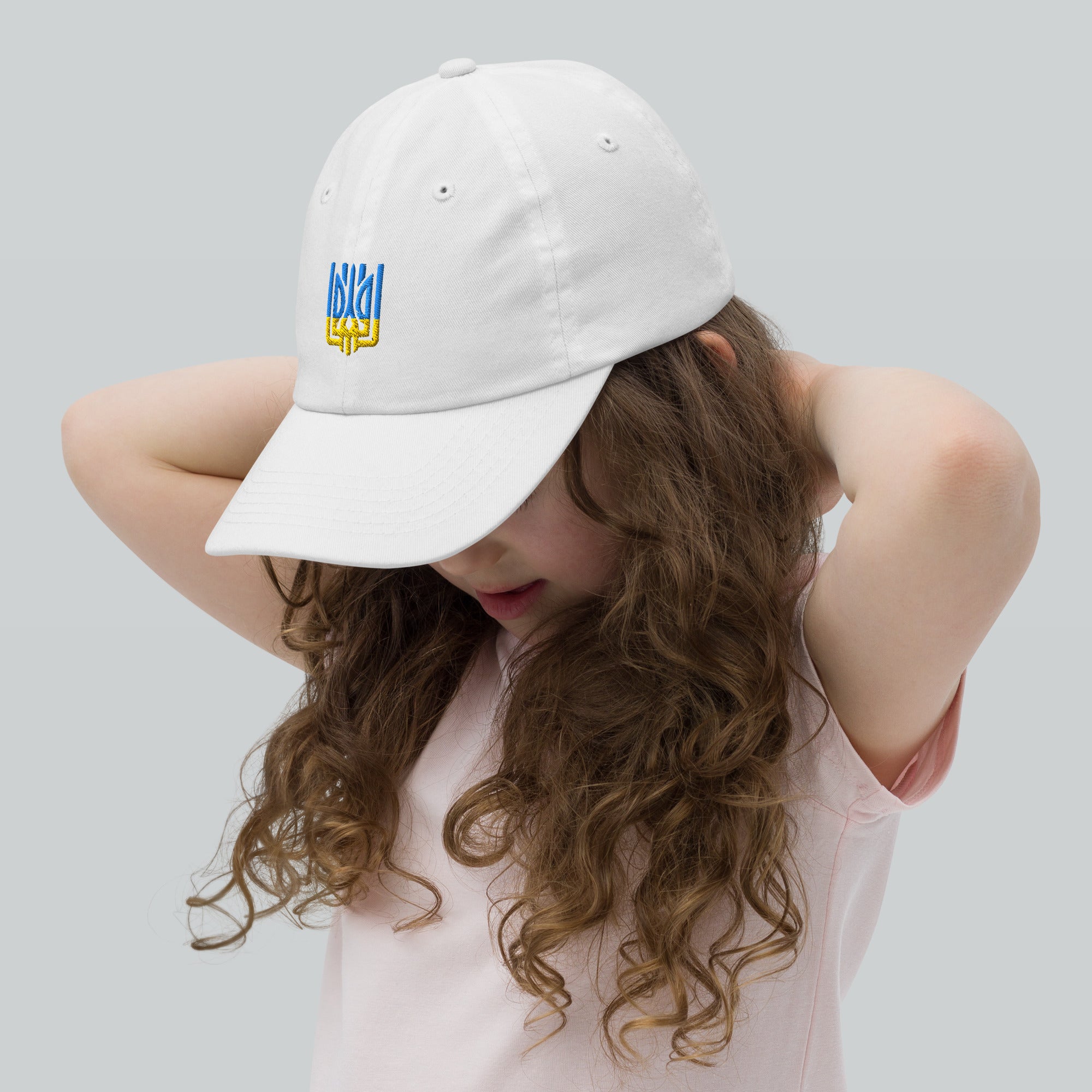 Child wearing a white youth baseball cap with a Ukrainian Tryzub emblem, showing breathable design and adjustable fit.
