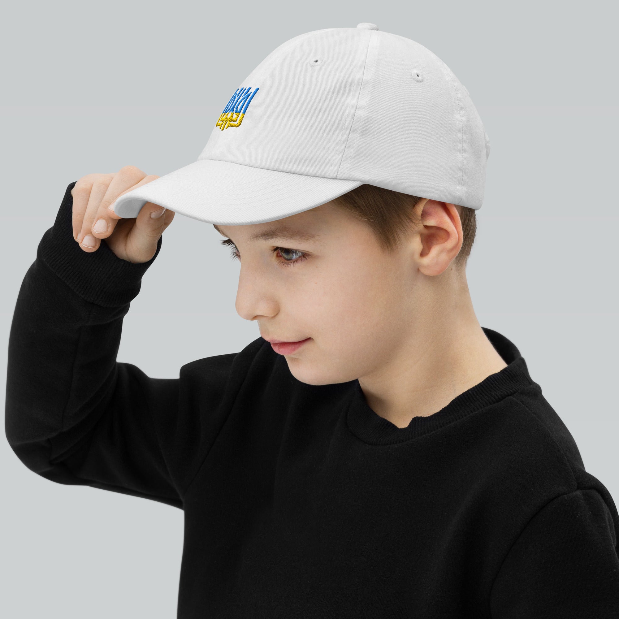 Young boy wearing a white youth baseball cap with Ukrainian Tryzub design, ideal for outdoor activities, made of breathable cotton.