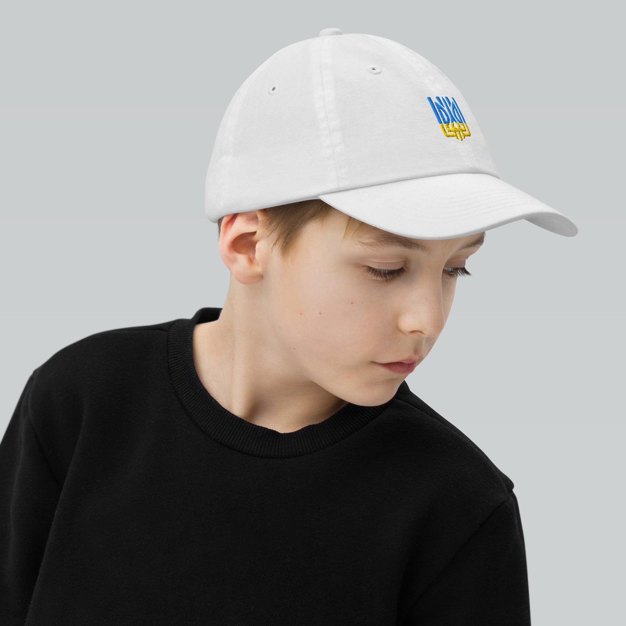 Youth wearing white baseball cap with Ukrainian Tryzub emblem, featuring breathable design and adjustable strap for active kids.