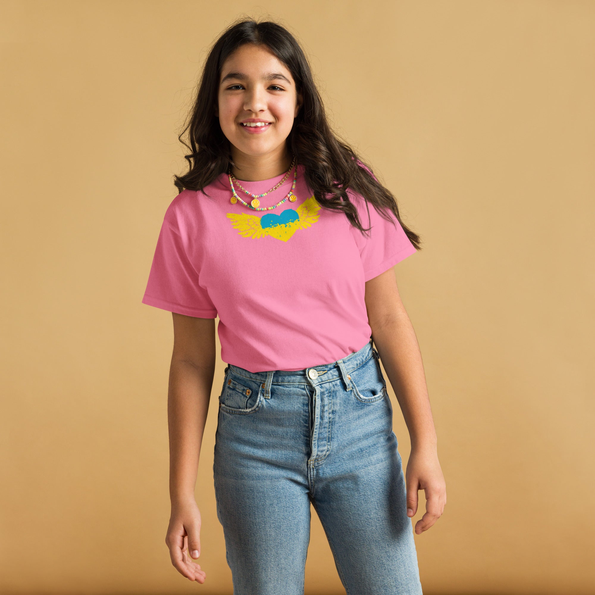 Youth wearing a pink t-shirt with Ukrainian emblem, jeans, and smiling against a beige background.