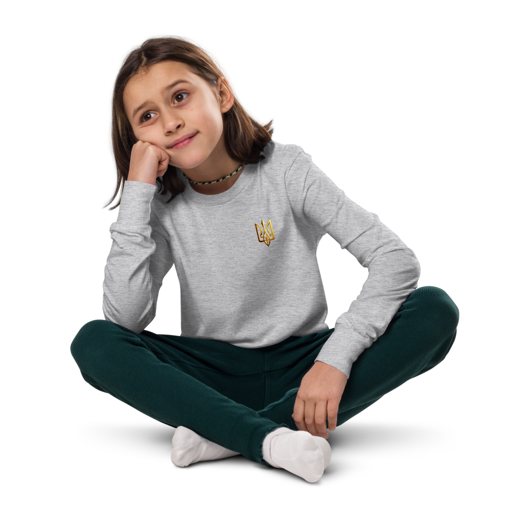 Youth wearing gray long sleeve shirt with golden Ukrainian Trizub design, sitting cross-legged on the floor.