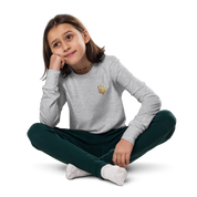 Youth wearing gray long sleeve shirt with golden Ukrainian Trizub design, sitting cross-legged on the floor.