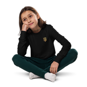 Youth wearing black long sleeve shirt with golden Ukrainian Trizub, sitting comfortably with legs crossed, showcasing cultural pride.