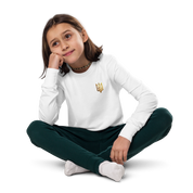 Youth wearing long sleeve shirt with golden Ukrainian Trizub on heart, sitting cross-legged, showcasing cultural heritage and style.